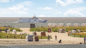A beach with portable cabins, a boat in the water, and a sandy area with people. - 1 bedroom amazing apartment in Büsum (Büsum)