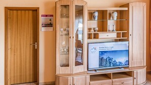 A wooden entertainment unit with a television displaying a mountain scene, a glass cabinet with wine glasses, and a door with a calendar. - 1 bedroom amazing apartment in Büsum (Büsum)
