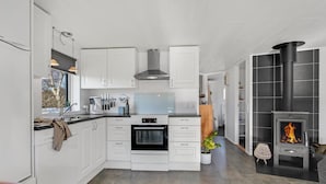 A modern kitchen with white cabinetry, a built-in oven, a stove, and a black tiled fireplace.