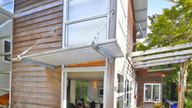 Ein modernes Haus mit Holzfassade, großen Fenstern und einer überdachten Terrasse mit Blumentöpfen.