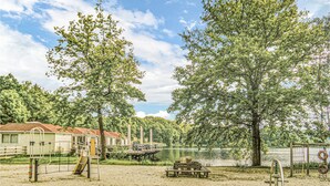 Un parque junto al lago con mesas de picnic, un área de juegos y un edificio de techo rojo.