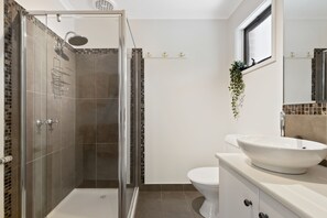 Un baño moderno con ducha envuelta en vidrio, un lavamanos blanco y un inodoro.