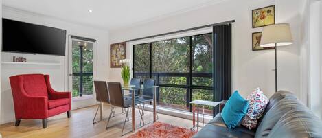Una sala de estar moderna con sofá, sillón rojo, mesa de comedor y sillas.