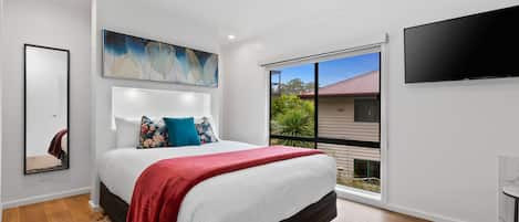 A modern bedroom with a large bed, a flat-screen TV, a painting, and a view of the outside.