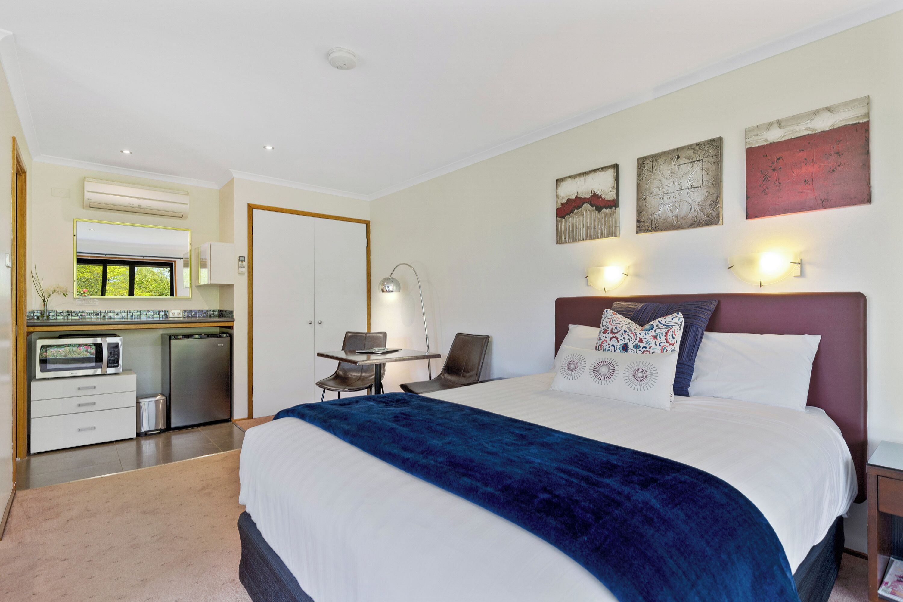 A modern bedroom with a large bed, bedside tables, a desk, and an air conditioning unit.