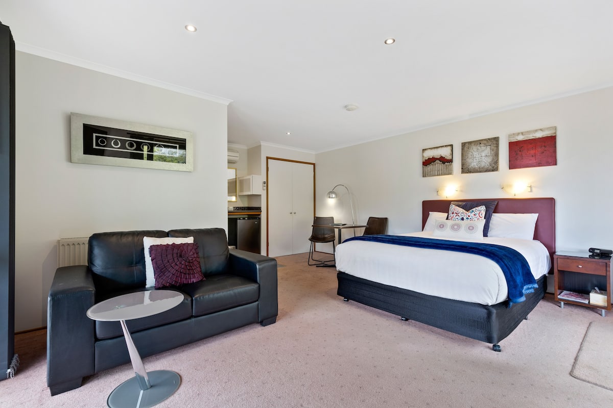 A hotel room with a bed, a sofa, a small table, a lamp, and artwork on the walls.