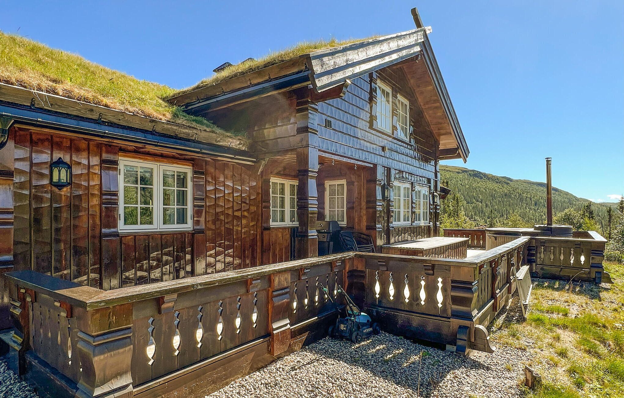A wooden chalet with a balcony, large windows, and a view of a forested mountain.