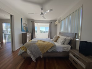 Relax in this serene bedroom with a large bed, ceiling fan, and natural light pouring in through the window.