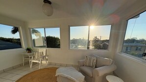 Ein sonnendurchflutetes Zimmer mit einer Couch, Hocker und kleinem Tisch, großen Fenstern und Blick auf die Stadt.