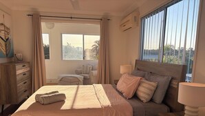 Ein Schlafzimmer mit einem großen Bett, Nachttischen, einer Kommode und einem Fenster mit Vorhängen.