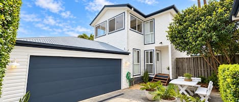 Une maison à deux étages avec un garage, une terrasse dotée de meubles d’extérieur et une variété de plantes en pot.