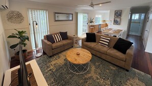 Ein großzügiges Wohnzimmer mit einer großen Couch, einem Couchtisch und einem Essbereich, im Hintergrund ist eine Küche zu sehen.
