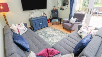 Una sala de estar con dos sofás grises, un televisor de pantalla plana, un mueble azul y una mesita de noche con una lámpara.