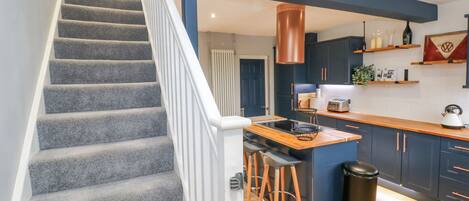 A modern kitchen with a central island, bar stools, and a trash can.