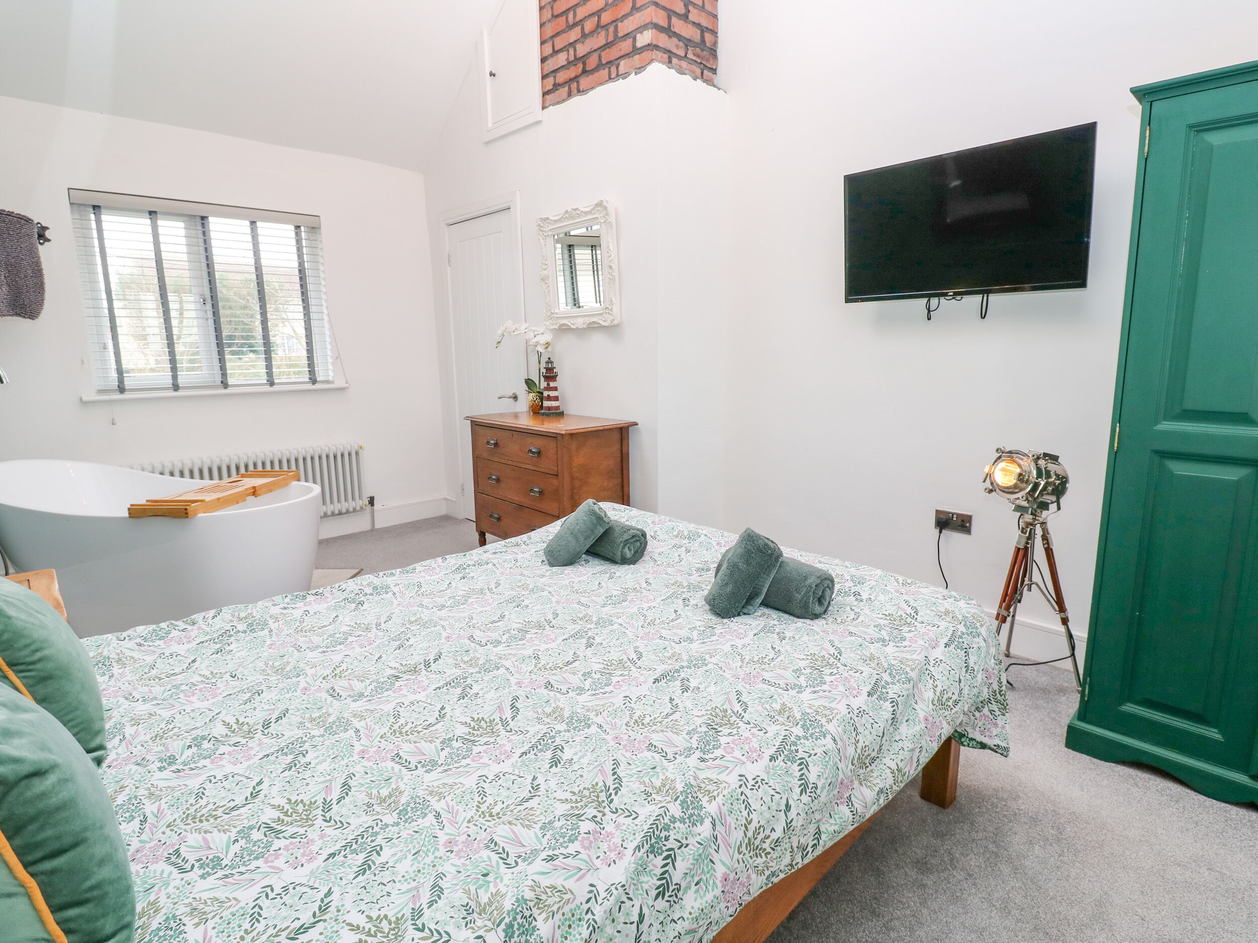 A bedroom with a bed, dresser, vanity, and a television.