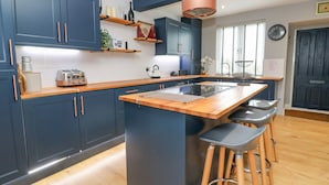 Et moderne køkken med mørkeblå skabe, en træbordplade og en central ø med barstole.