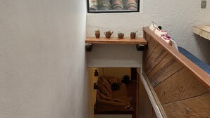 A narrow stairway with a wooden handrail, a small window with a view of a tiled roof, and a shelf with three small pots. - PiYo (San Cristóbal de las Casas)