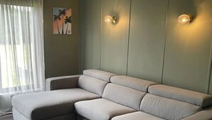 Ein modulares Sofa mit passendem Hocker in einem Raum mit hellgrünen Wänden und zwei Wandleuchten.