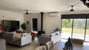Ein modernes Wohnzimmer mit zwei Sofas, einem Fernseher, einem Kamin und einem großen Fenster mit Blick auf Grünflächen.