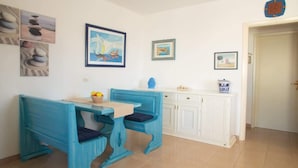 Une pièce avec un banc et une table bleus, des armoires blanches et divers tableaux encadrés accrochés aux murs.