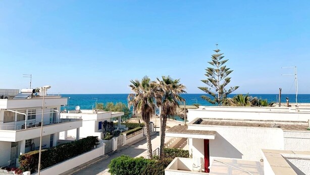 Un quartier résidentiel en bord de mer, avec des bâtiments modernes, un palmier et une vue dégagée sur la mer.