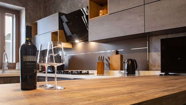 A modern kitchen with a wooden countertop, a wine bottle, and glasses.