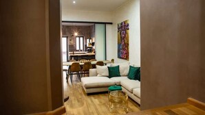 A modern living room with a sectional sofa, a dining area with chairs, and a kitchen in the background.