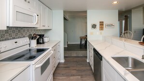 Een keuken met witte kastjes, een magnetron, fornuis, vaatwasser en een spoelbak.