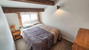 Ein Schlafzimmer mit einem Bett, einem Nachttisch, einer Lampe und einem Holzkasten.