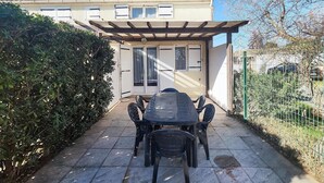 Eine Terrasse mit Tisch und Stühlen, einer Pergola und einem Gebäude mit Ziegeldach und Fenstern.