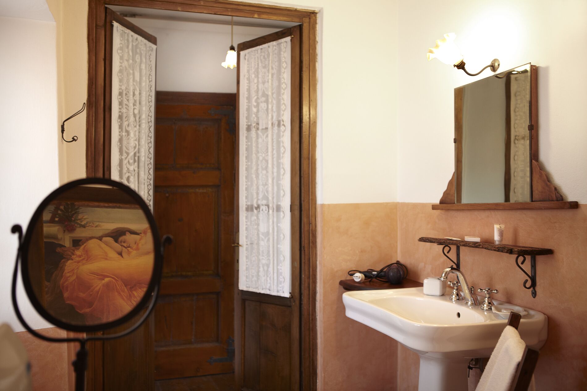 Un baño con puerta de madera, un lavabo blanco, un espejo y un estante en la pared.