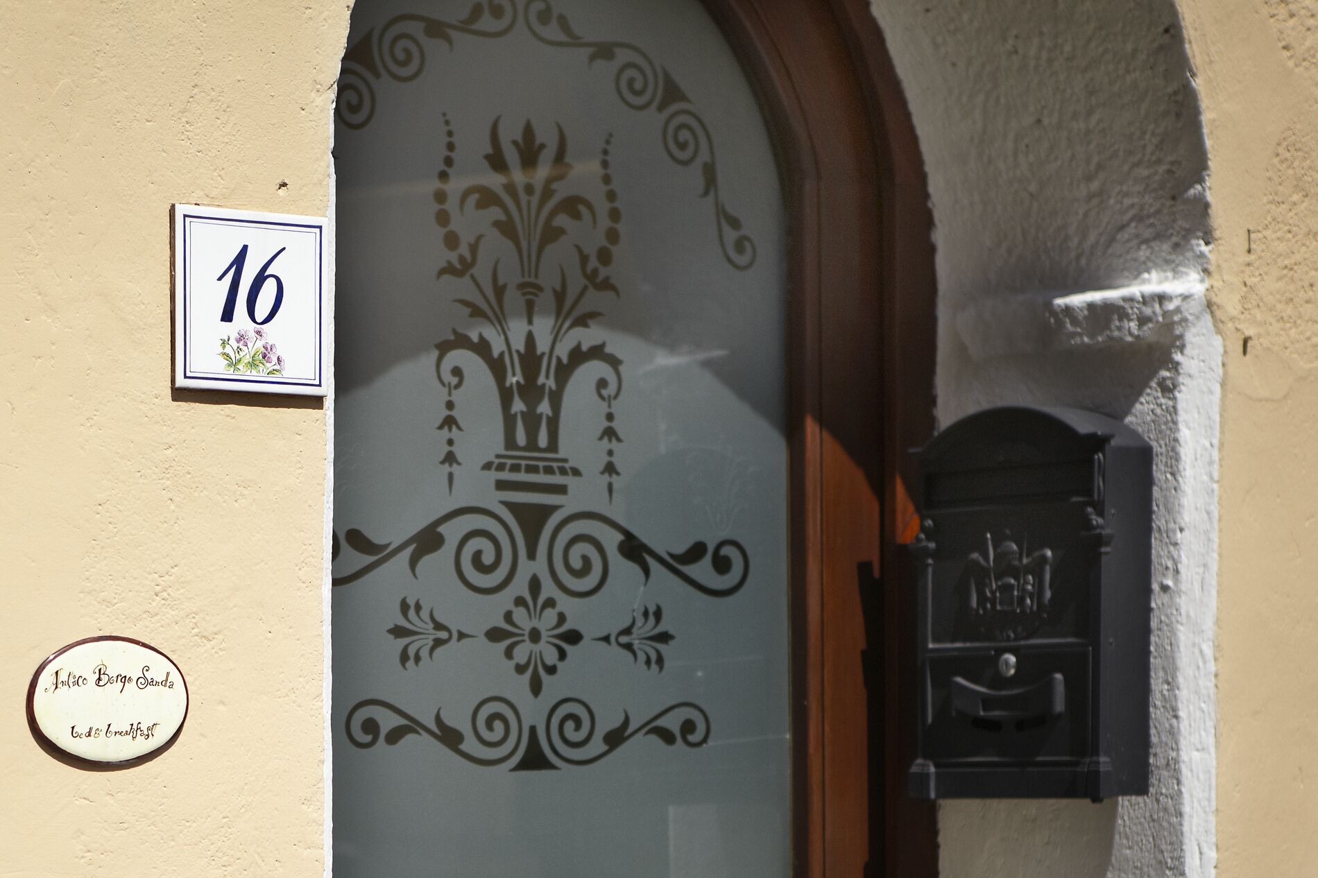 A building entrance with a decorative glass door, a mailbox, and a house number sign.