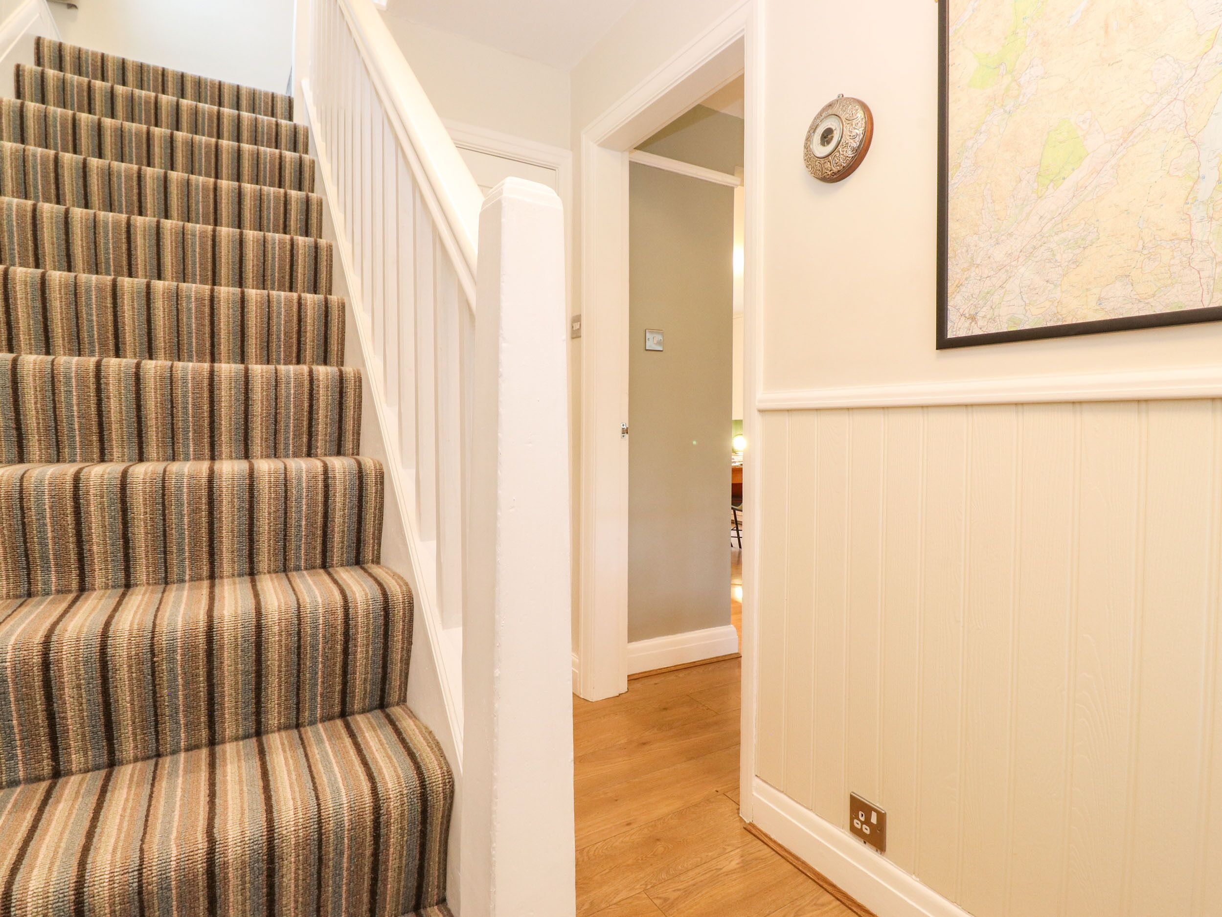 A staircase with striped carpet, a wall-mounted map, and a door leading to another room.