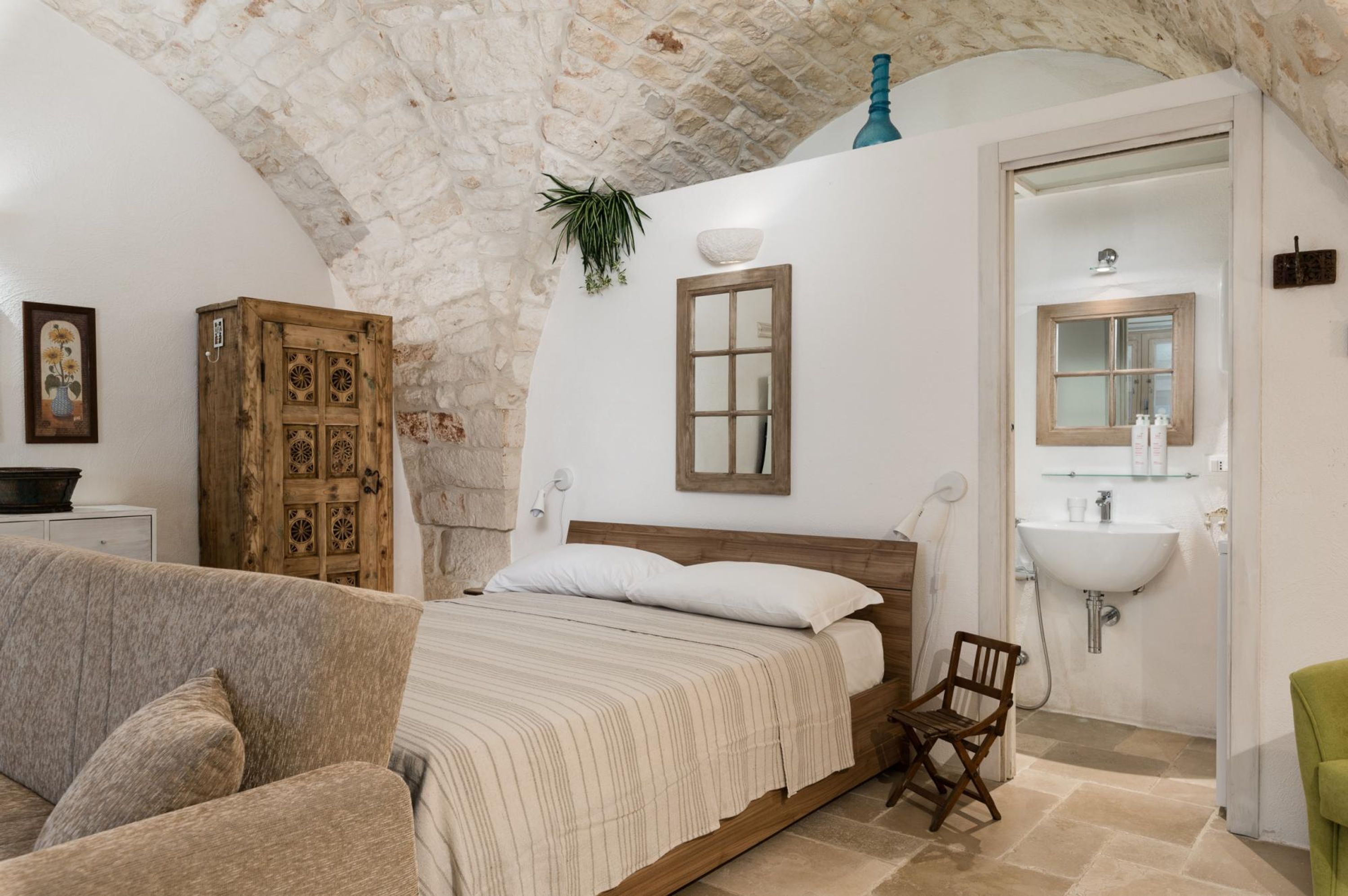 Una camera da letto con soffitto in pietra, un letto di legno, una poltrona accanto al letto, un lavandino bianco e uno specchio.