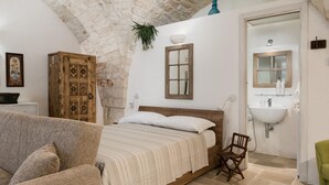 A bedroom with a stone ceiling, a wooden bed, a bedside chair, a white sink, and a mirror.