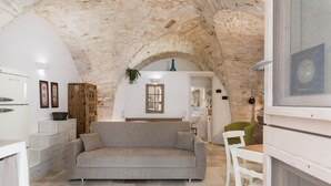A cozy living room with a stone ceiling, a grey sofa, white furniture, and a wooden cabinet.