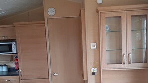 A compact kitchen with a microwave, cabinets, and a small refrigerator. - Northfield 198, Skipsea Sands (Driffield)