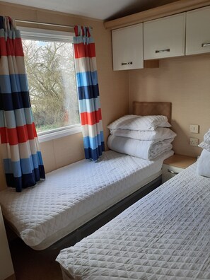 Uma cama de solteiro com colchão branco acolchoado, cabeceira e janela com cortinas listradas.