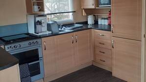 A compact kitchen with a gas stove, oven, microwave, and a small window. - Northfield 198, Skipsea Sands (Driffield)