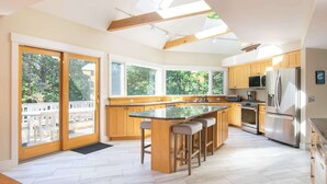 Una cocina moderna con gabinetes de madera, una isla central con taburetes, un refrigerador de acero inoxidable y ventanas amplias.