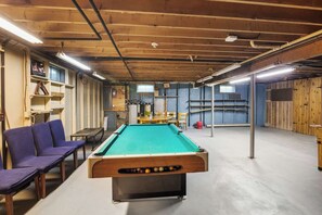 A pool table in a room with wooden beams, a table with chairs, and shelves against the wall.