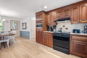 A modern kitchen with wooden cabinets, a stainless steel stove, and a dining area with a white table and chairs.
