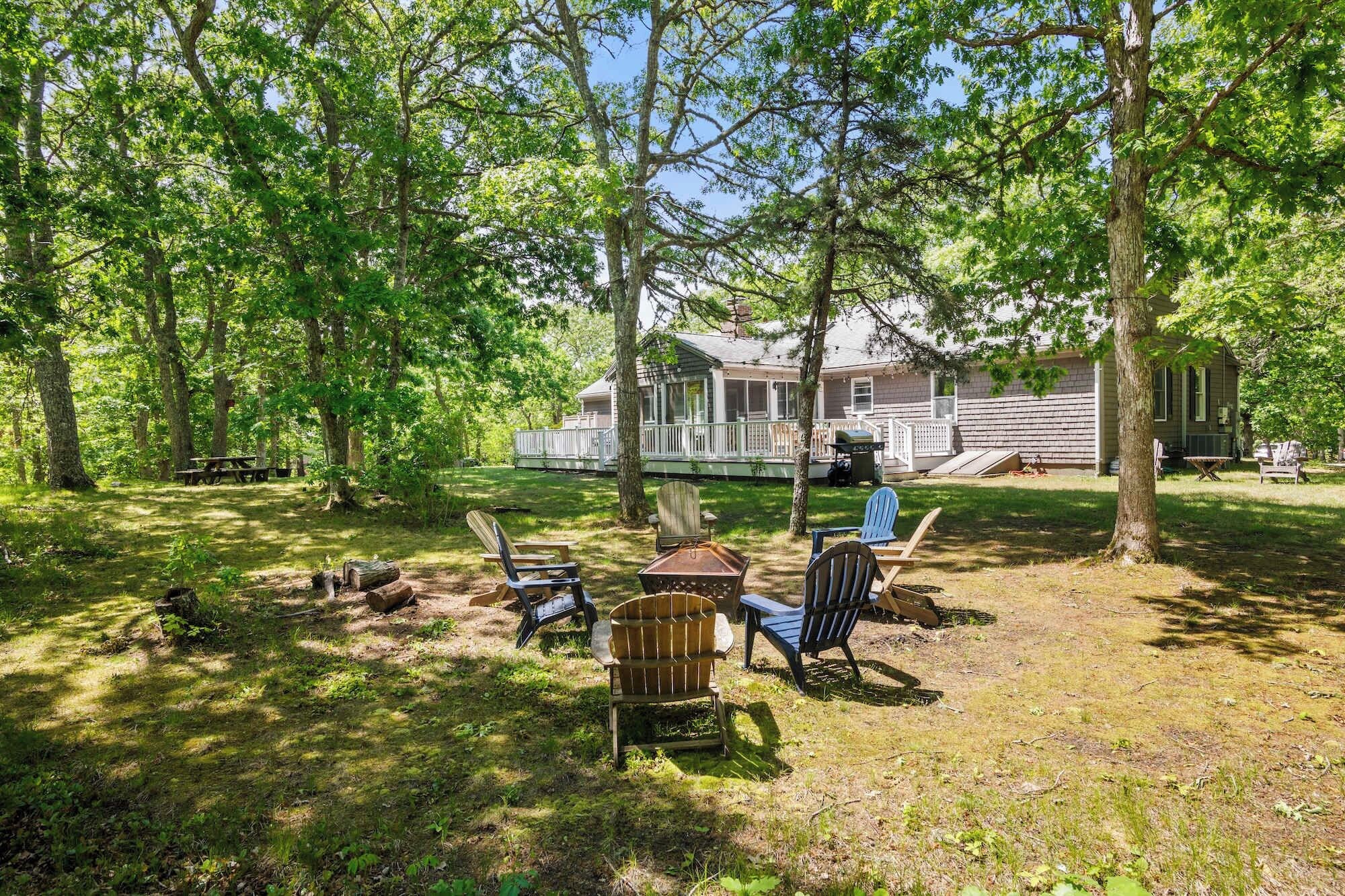 A backyard with a wooden deck, picnic table, and several Adirondack chairs.