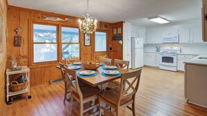 A wooden-paneled dining room with a table set for four, a kitchen with white appliances, and a chandelier. - 12 42nd Avenue by Avantstay 2 Mins To The Beach Screened In Porch! (Isle of Palms)