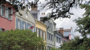 A row of colorful buildings with shutters, a flag, and trees in the foreground. - 12 42nd Avenue by Avantstay 2 Mins To The Beach Screened In Porch! (Isle of Palms)