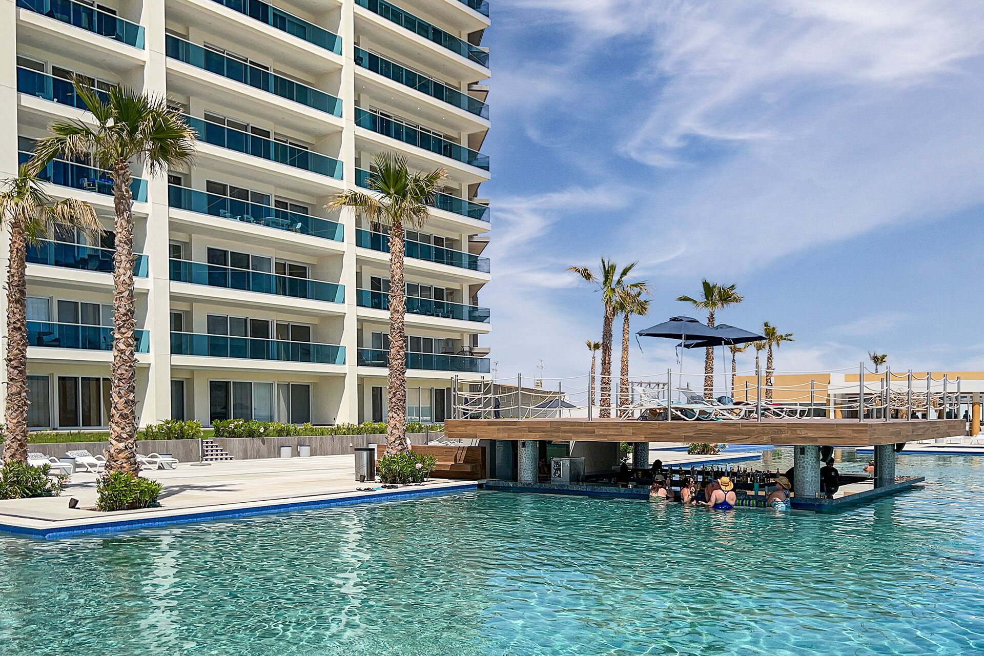 A hotel with a pool area, palm trees, and a multi-story building with balconies.