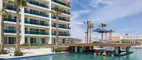 A hotel with a pool area, palm trees, and a multi-story building with balconies.