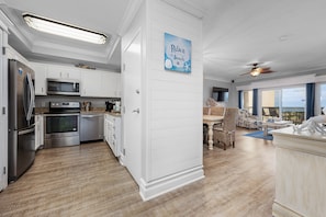 A modern kitchen with white cabinetry, stainless steel appliances, and a blue seaside-themed wall hanging.