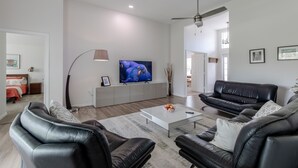 A modern living room with a white sofa, black leather armchairs, a coffee table, and a flat-screen TV on a white cabinet. - Welcome at Coastal Soul perfect place for traveling Family  (Vero Beach)
