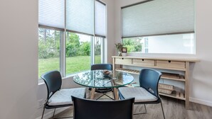 A modern room with a glass table, four chairs, a wooden desk, and large windows with blinds. - Welcome at Coastal Soul perfect place for traveling Family  (Vero Beach)